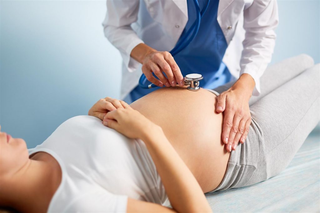 enfermeira com estetoscópio sobre a barriga da grávida