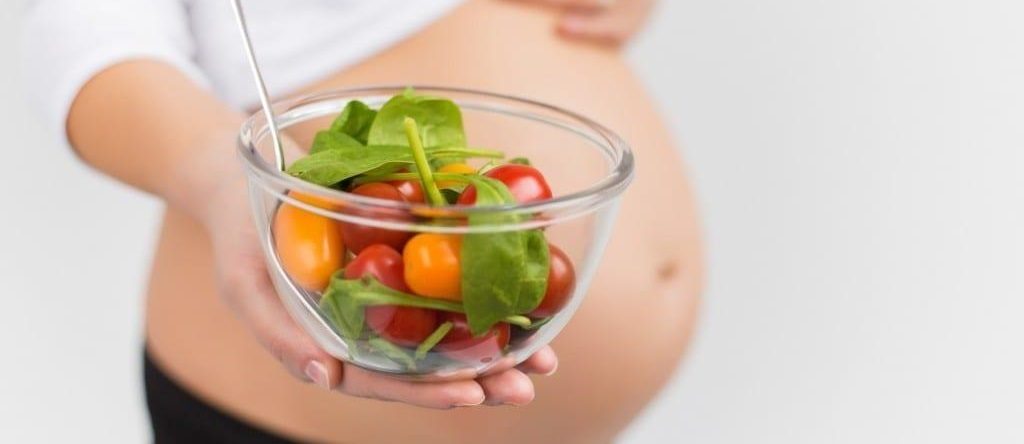 grávida segurando prato com legumes e verduras